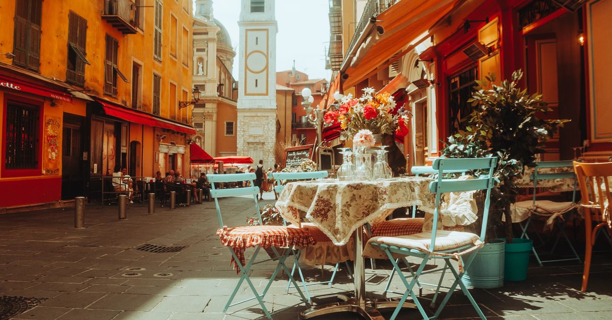 A sunny French café terrace with tables and chairs on a cobblestone street.