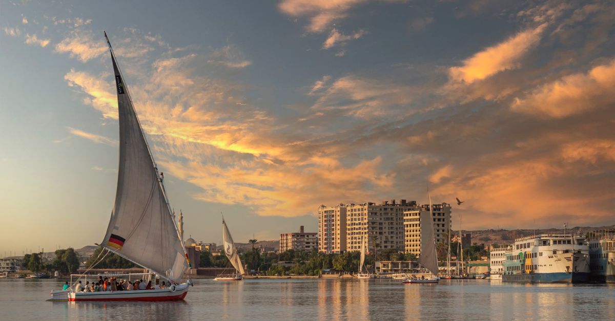A traditional felucca sailboat on the Nile at sunset with a city skyline in the background.